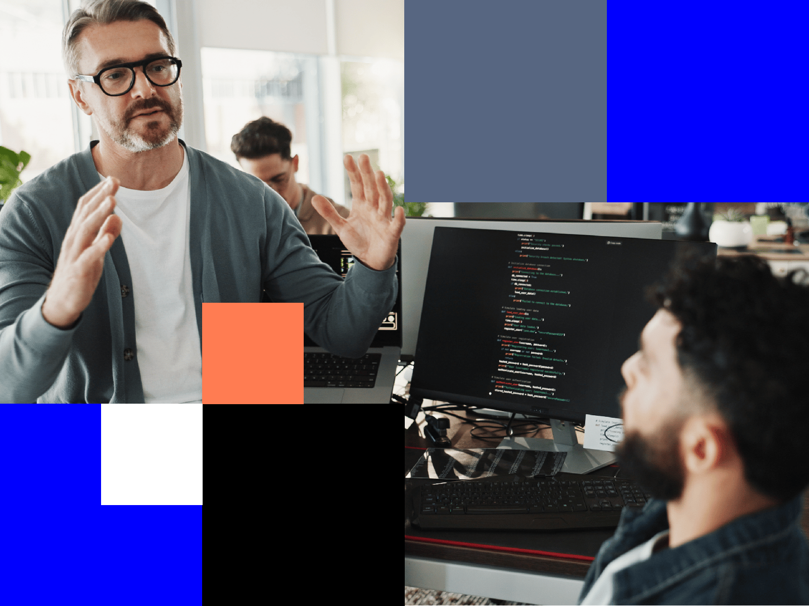 A man gestures while speaking to another man in front of a computer screen